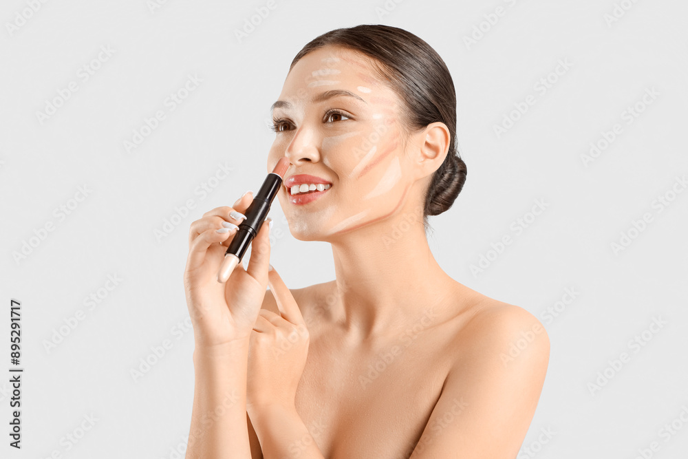 Young Asian woman with contouring and makeup stick on light background, closeup