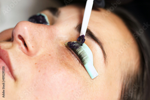 Fotografie A beautician in black gloves uses a brush to apply lash tint to a woman's eyelashes