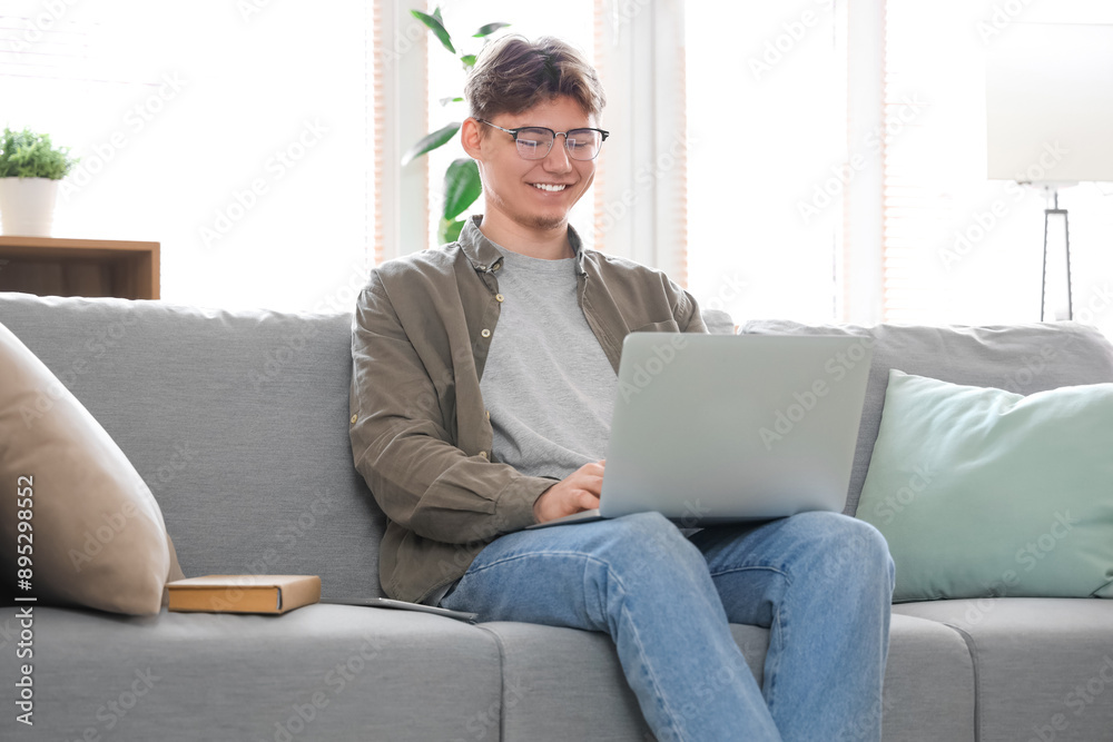 Male student with laptop studying online on sofa at home Male student with laptop studying online on sofa at home