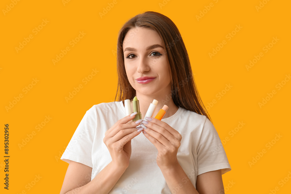 Beautiful young woman with row of lip balms on yellow background Beautiful young woman with row of lip balms on yellow background