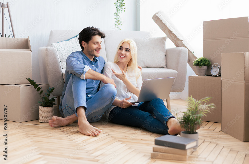 Couple Sitting With Laptop Computer On Floor In New Flat Relaxing After Moving House. Copy Space Couple Sitting With Laptop Computer On Floor In New Flat Relaxing After Moving House. Copy Space