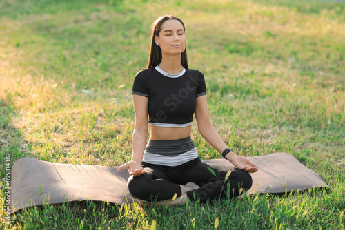 Sporty young woman meditation on yoga mat in park