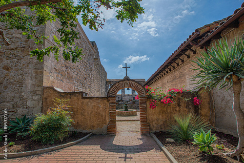 California, USA - October 2, 2017: Low angle and front view of arch entrance door with The Cross and red flowers at Mission San Juan Capistrano
 photo