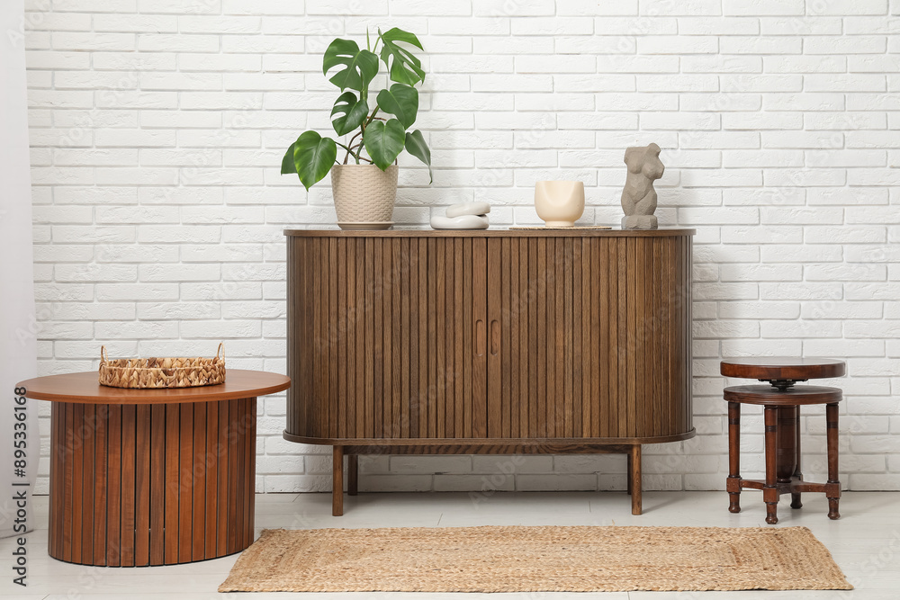 Stylish chest of drawers with plant, decor and coffee tables in room