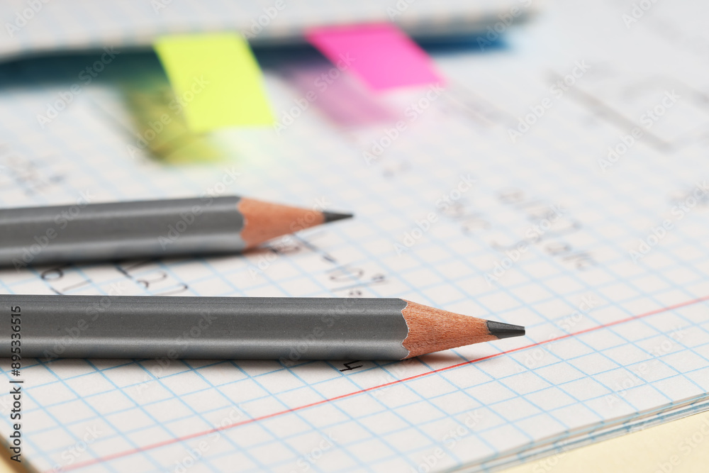 Copybook with handwritten maths formulas with pencils on yellow background, closeup Copybook with handwritten maths formulas with pencils on yellow background, closeup