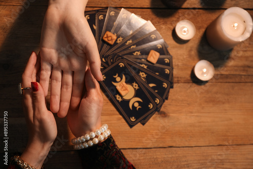 Bild auf Leinwand Fortune teller reading lines on woman's palm at wooden table, top view
