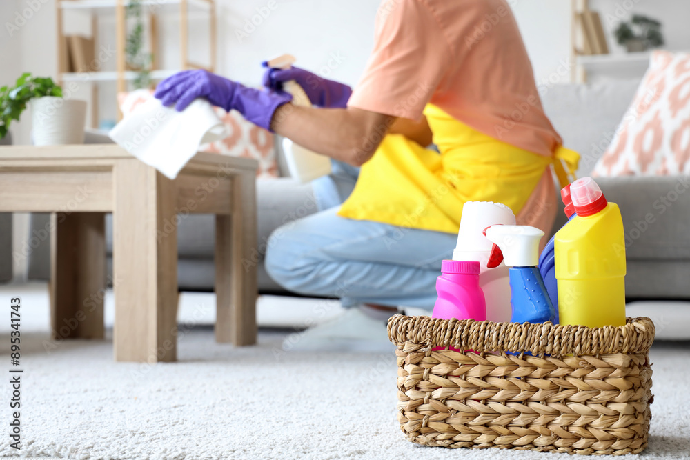 Male janitor near basket with cleaning supplies in light room Male janitor near basket with cleaning supplies in light room