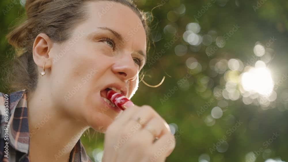 Woman Licks a Striped Popsicle, Relishing the Sweet Treat in the Sun's Rays. Woman Licks a Striped Popsicle, Relishing the Sweet Treat in the Sun's Rays.