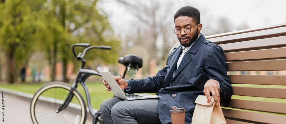 An African American businessman works on his laptop on a park bench, with a bicycle nearby. The mood is serene and productive, merging nature with professional duties. An African American businessman works on his laptop on a park bench, with a bicycle nearby. The mood is serene and productive, merging nature with professional duties.