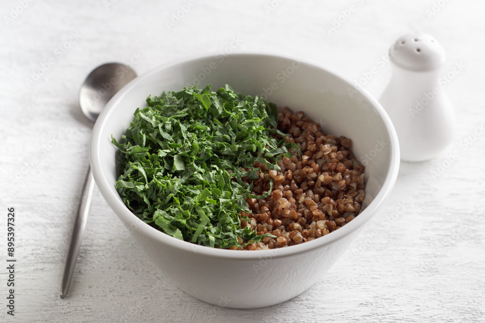 White bowl with boiled buckwheat and kale on a gray background, top view. Healthy homemade vegan food White bowl with boiled buckwheat and kale on a gray background, top view. Healthy homemade vegan food