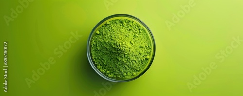 Vibrant green matcha powder in a clear bowl on a green background, showcasing the fine texture and bright color of the powdered tea.