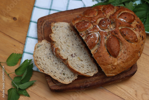 Top view of Baked homemade round bread cut in slices with nettles on wooden table with fresh nettle plants photo