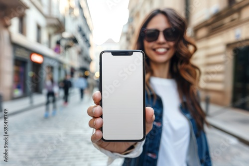 Young woman showing a blank smartphone screen in the city, ready for your app or message, highlighting urban lifestyle and technology