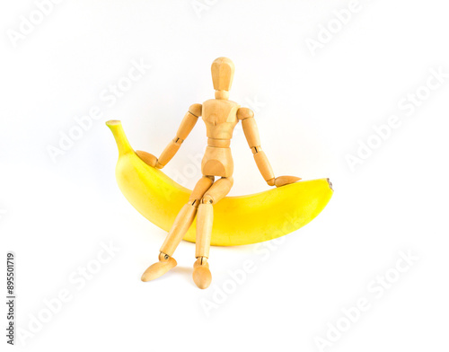 A wooden mannequin sitting on banana, Isolated, White background