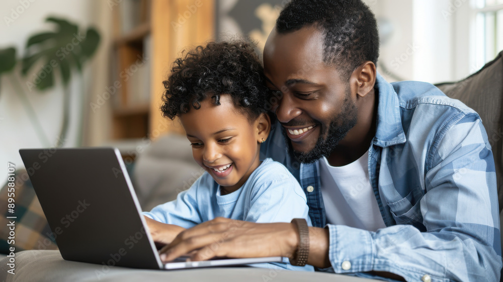 A father and child smiling while working on a school project on a laptop in the living room. A father and child smiling while working on a school project on a laptop in the living room.