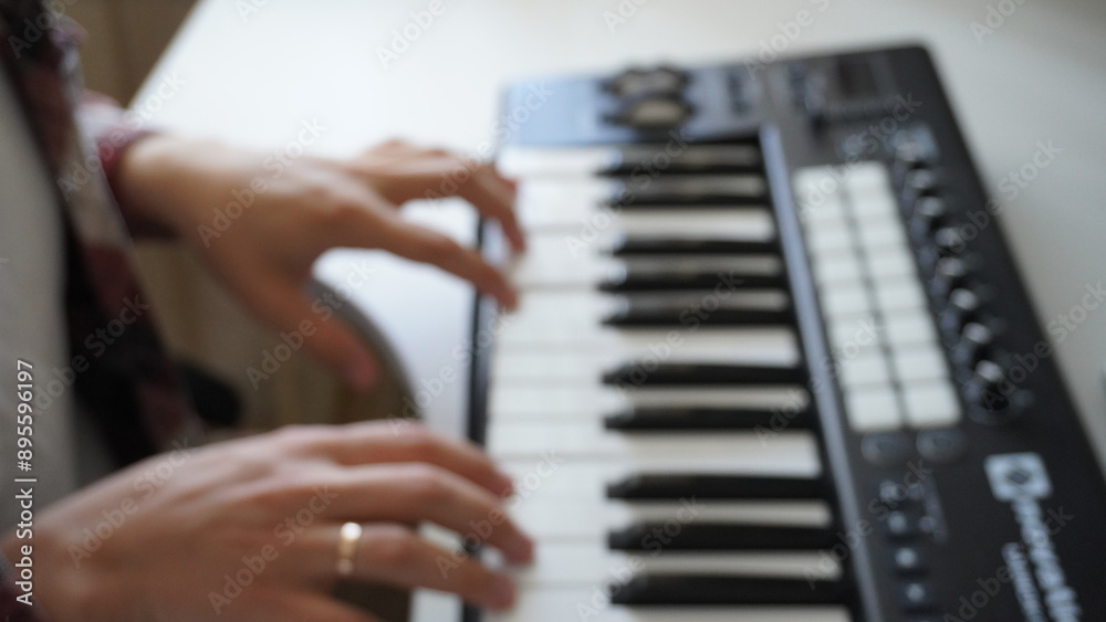 Obraz premium Recording music notes, playing electronic keyboard, midi keys in music sequencer. Hands and midi controller on the table, man composing music, blur