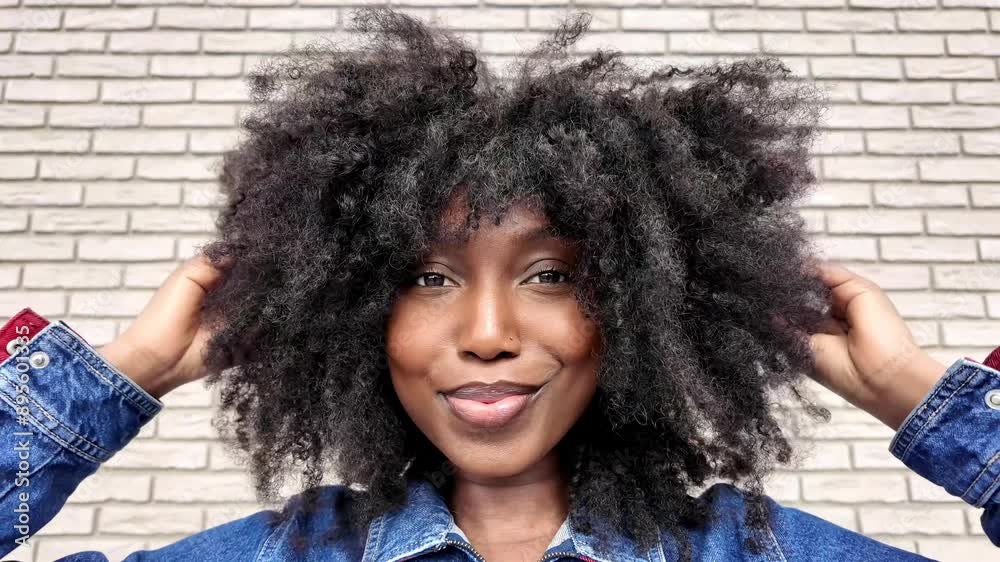 Confident woman flaunts trendy look with afro hairstyle and denim jacket against brick wall backdrop Confident woman flaunts trendy look with afro hairstyle and denim jacket against brick wall backdrop