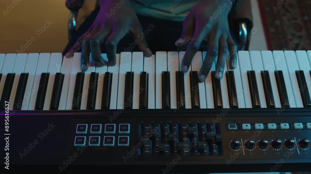 Close-up top down shot of hands of professional musician playing keyboard and adjusting synthesizer settings in recording studio