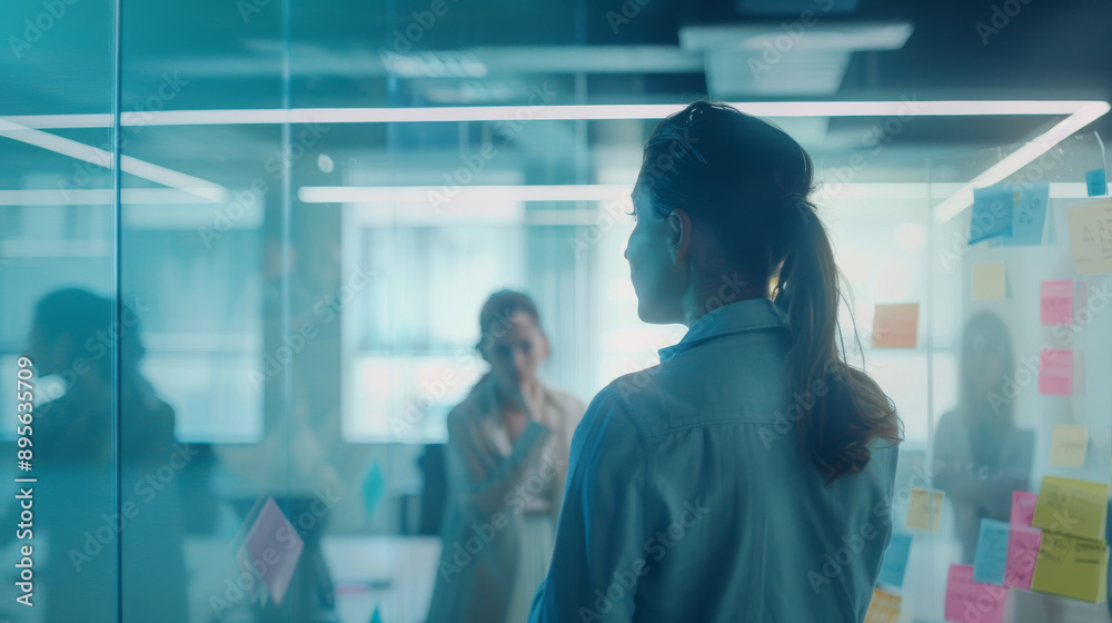 A thoughtful woman looks at colorful sticky notes on a glass wall, brainstorming ideas in a modern, luminous office space. A thoughtful woman looks at colorful sticky notes on a glass wall, brainstorming ideas in a modern, luminous office space.