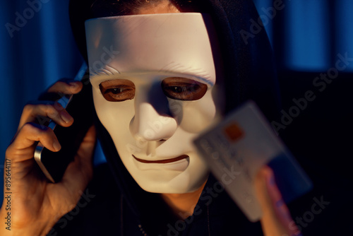 White criminal anonymous mask calling to credit card owner to threaten ransom with privacy information all database, making password encryption by programming hack trying to make insecure. Pecuniary. photo