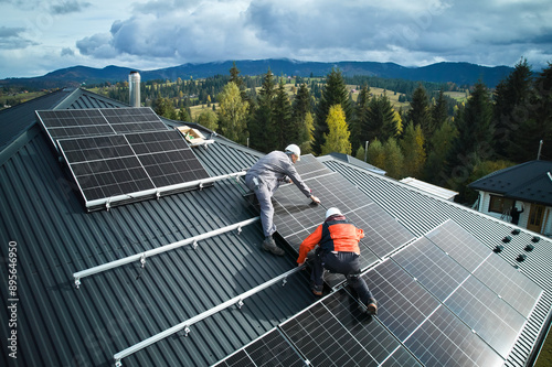 Electricians building photovoltaic solar module station on roof of house. Men technicians in helmets installing solar panel system outdoors. Concept of alternative and renewable energy. Aerial view. photo