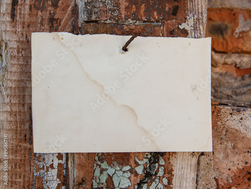 Old vintage paper advertisement hanging on aged wall nailed by rusty doornail photo