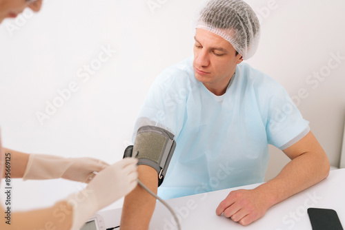 Close-up cropped shot measuring blood pressure of man patient during examination in medical clinic. Doctor female checking patient arterial blood pressure. Male patient having blood pressure checked