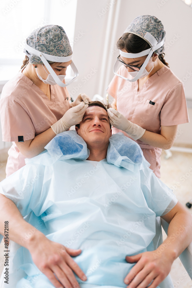 Vertical shot of female trichologist surgeons carry out hair transplant surgery in operating room to male patient with hairloss problem. Surgical technique that moves hair follicles from part of head.