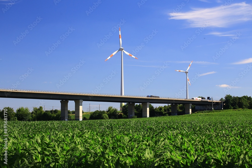 Wind turbines beside German Autobahn bridge over green field under clear blue sky