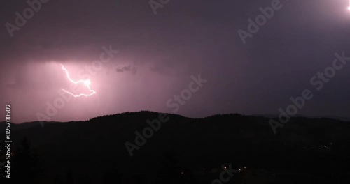 Lightning storm in the night sky at mountain. Multiple lightnings and thunders illuminate night sky and hills with firs