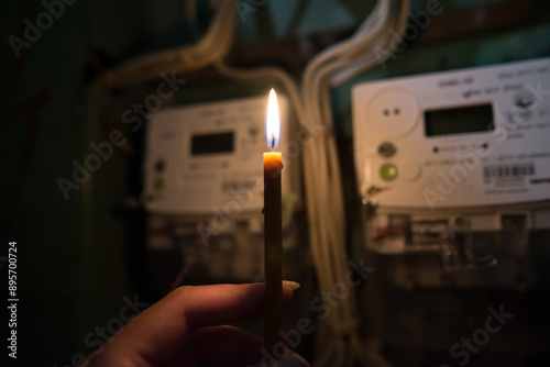 a hand with a candle in complete darkness looks at the electricity meter at home. photo