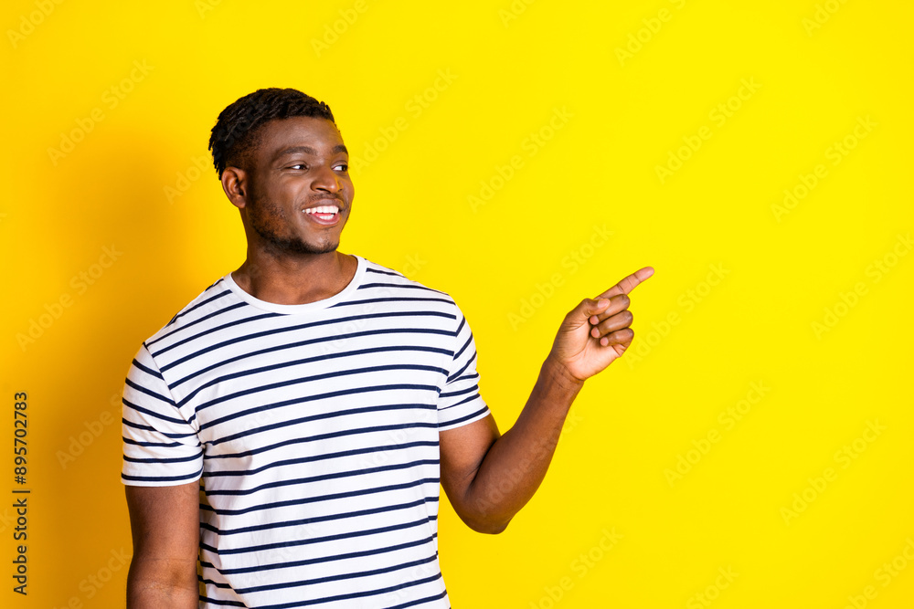 Photo of nice young man direct fingers empty space wear striped t-shirt isolated on bright yellow color background Photo of nice young man direct fingers empty space wear striped t-shirt isolated on bright yellow color background