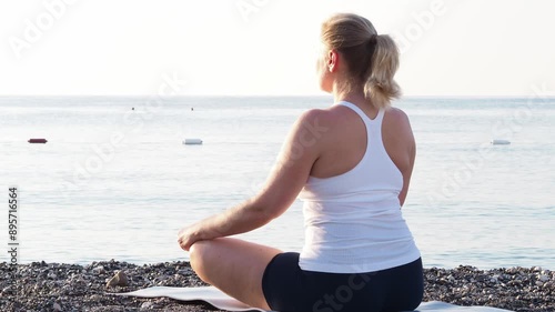 A calm woman takes a deep breath, enjoys the fresh air, meditates with her eyes closed, sitting on the seashore. practice mental relaxation. The practice of relaxation and unity with nature