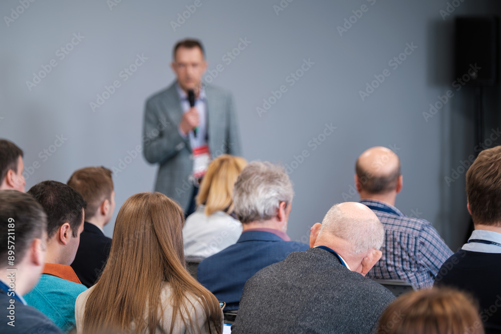 Fototapeta premium Business professionals attentively listening to a speaker at a conference. Audience members focused on presentation, learning and networking.