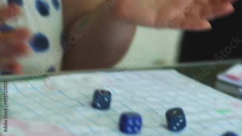 A woman playing a Yahtzee game throwing dice on a table closeup and writing the score photo