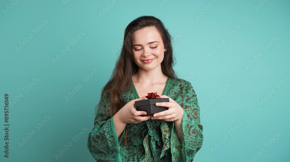 Happy young woman receiving gift box in blue studio