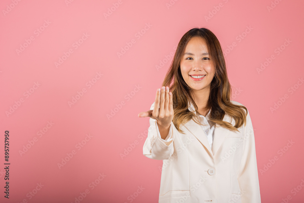 Happy Asian portrait beautiful cute young woman teen smile positive friendly making gesture hand inviting to come here with hand look to camera studio shot isolated on pink background with copy space