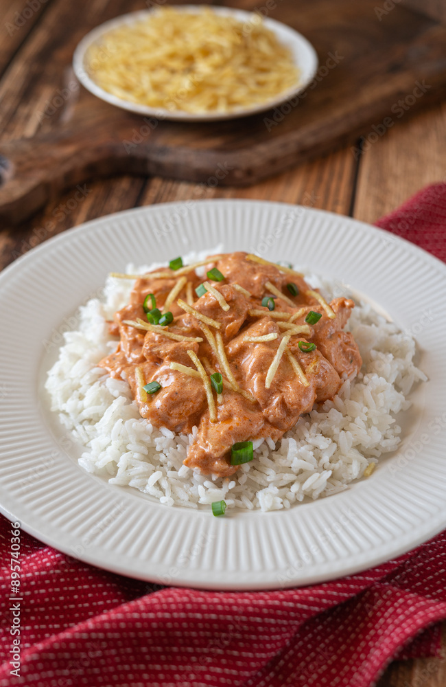 Brazilian style Chicken strogonoff with rice and potato straw on wooden table.