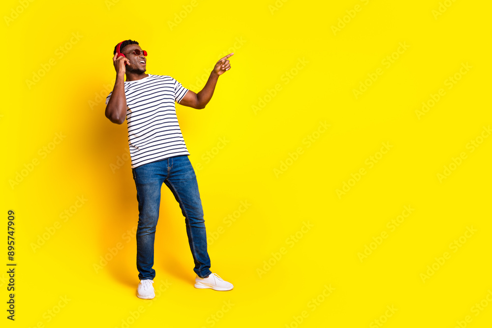Fototapeta premium Full body portrait of nice young man headphones point finger empty space wear t-shirt isolated on vibrant yellow color background