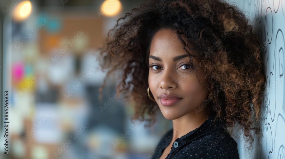 Woman with curly hair and hoop earrings smiling confidently indoors against a blurred background. Woman with curly hair and hoop earrings smiling confidently indoors against a blurred background.