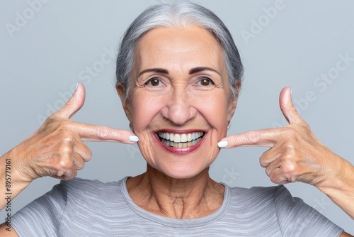 An elderly woman with gray hair joyfully points to her pearly white teeth and shows wide and bright smile photo