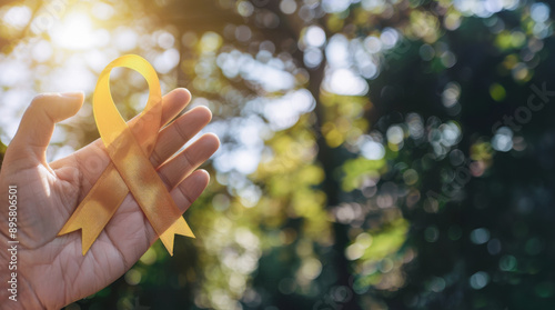 Close-up of a hand holding a yellow ribbon in sunlight with a blurred green background symbolizing support, awareness, and Suicide Prevention Day photo