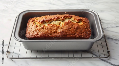 Freshly Baked Banana Bread in Loaf Pan A loaf of banana bread in a nonstick pan resting on a wire cooling rack