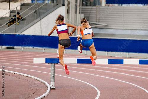 3000 metres steeplechase, two women synchronously overcome barrier photo