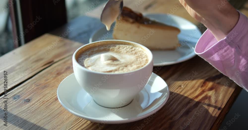 Woman stirs decorative foamy coffee drink at breakfast in coffeeshop closeup. Female takes spoon with dripping froth out of beverage at wooden table
