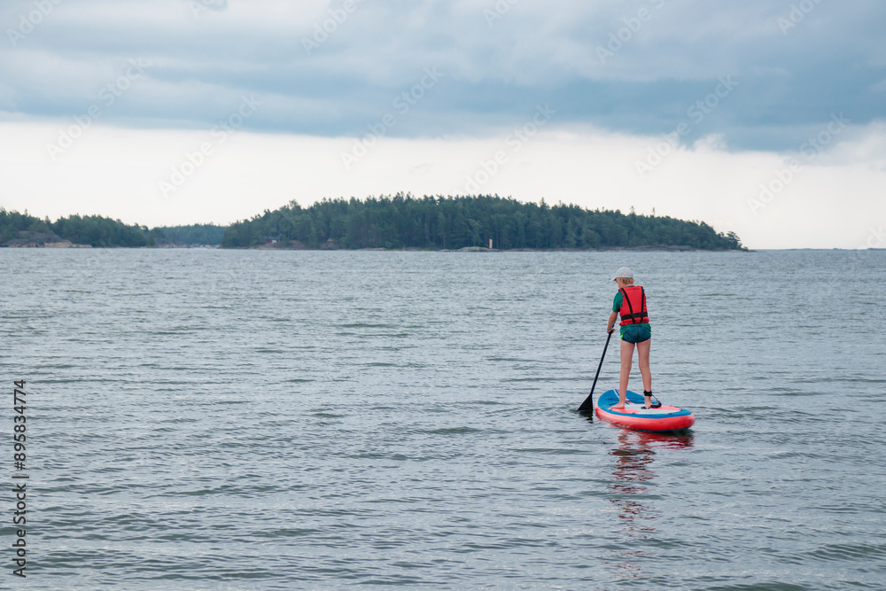 Naklejka premium Little boy paddling on a paddle surfboard sup board in Baltic sea, Gulf of Finland, kids vacation, summer holidays in Finland