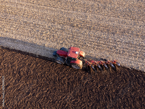 Red tractor working in the field on sunrise. Plowing field in early spring with tractor, concept of agriculture and farming