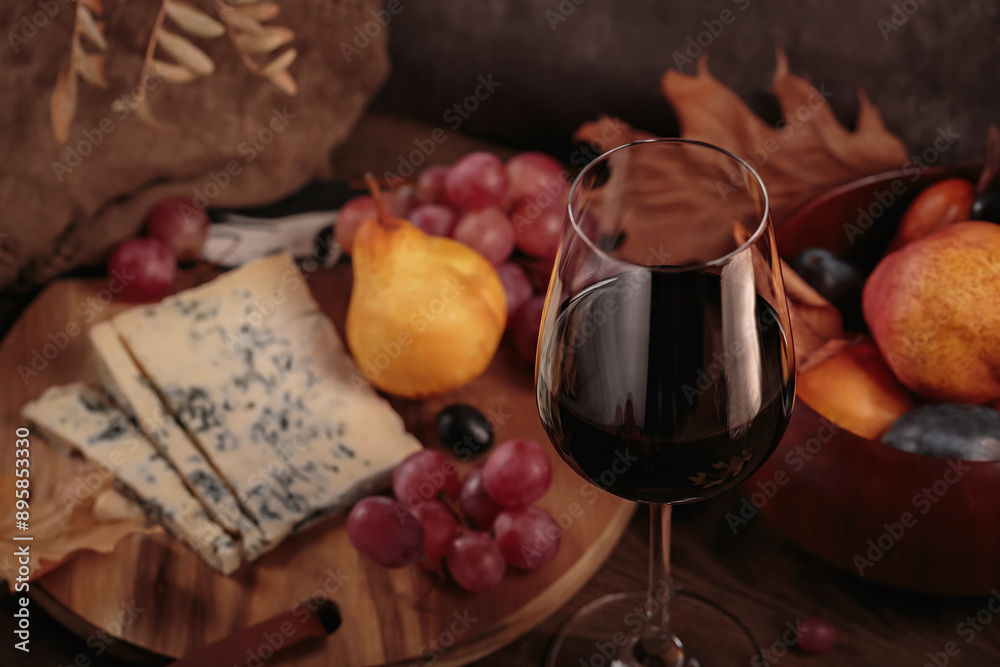 Glass of red wine served with blue cheese on dark wooden background. Autumn picnic with wine and cheese platter, fruits and dry leaves in rustic style Glass of red wine served with blue cheese on dark wooden background. Autumn picnic with wine and cheese platter, fruits and dry leaves in rustic style