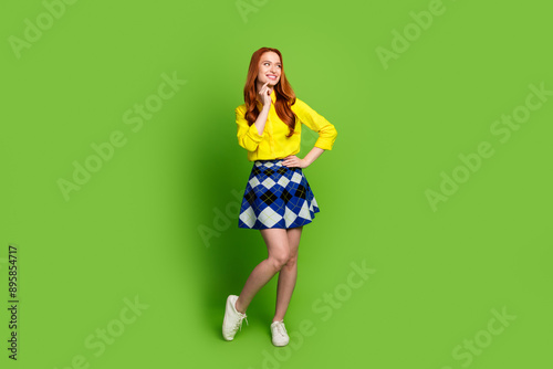 Full length photo of lovely young lady look empty space minded dressed stylish yellow garment isolated on green color background