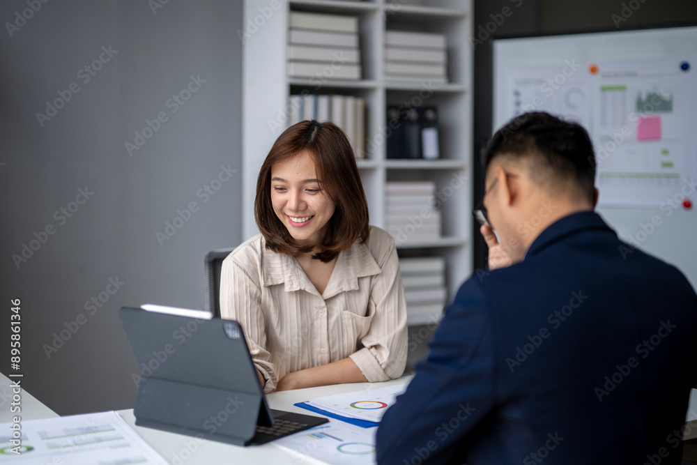 A woman and a man are sitting at a desk with a laptop and a tablet A woman and a man are sitting at a desk with a laptop and a tablet